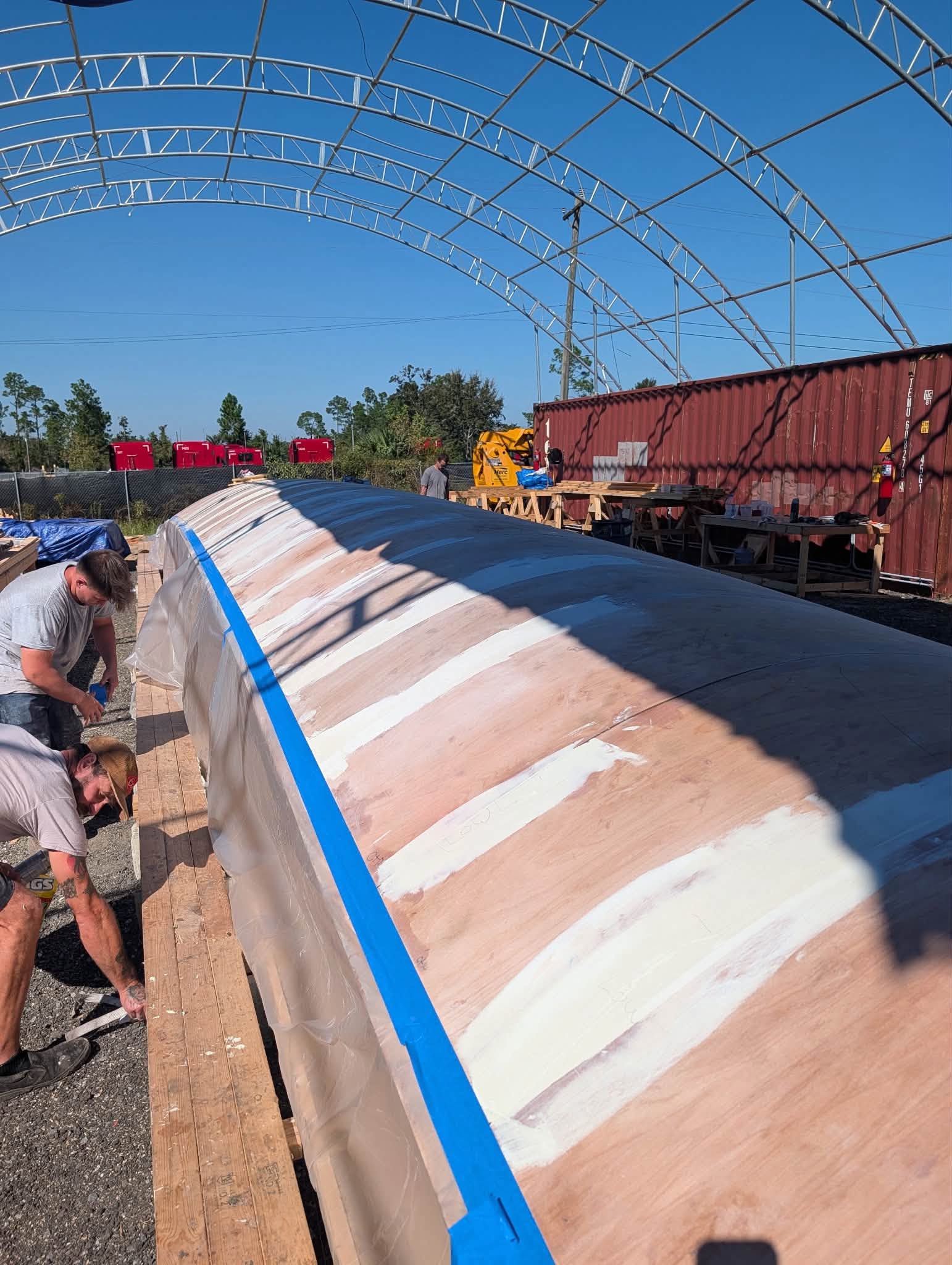 Two crew fairing the hull mold under the tent frame